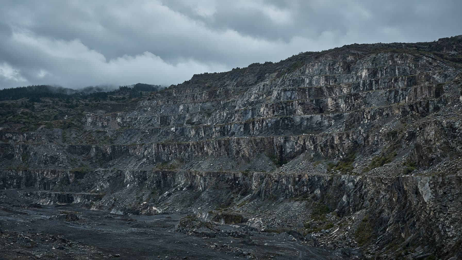 A wide quarry cut into a hillside, terraced rock faces rising in steps under overcast light.